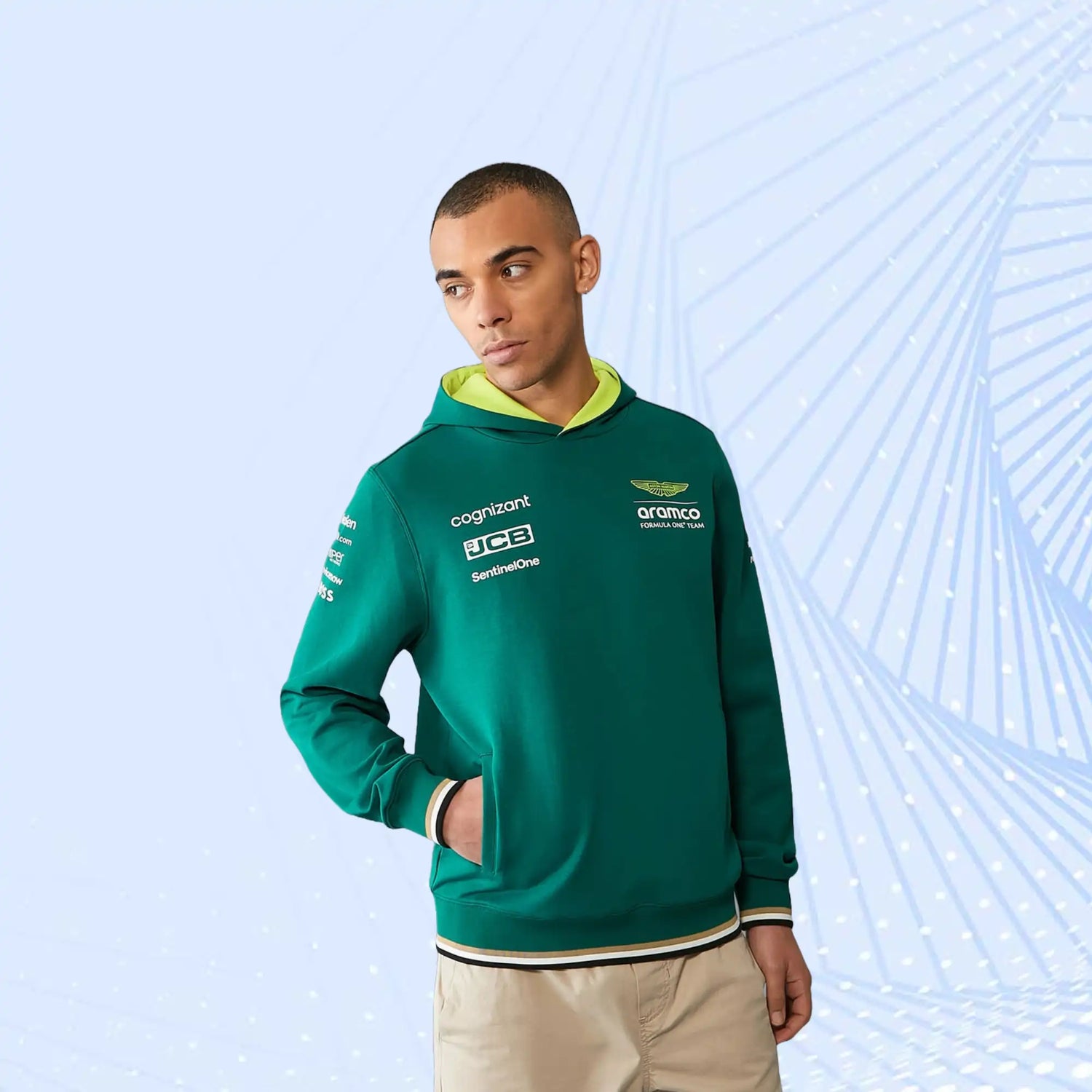 A person wearing a green Aston Martin F1 Team hoodie with sponsor logos, a hood, and a kangaroo pocket, standing against a patterned background.